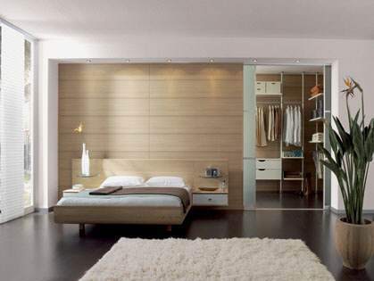 Modernes Schlafzimmer mit begehbarem Kleiderschrank, Holzwand und großem Teppich.